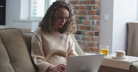 Happy woman sitting on couch using her laptop at home in the living room Stock Footage 154714931