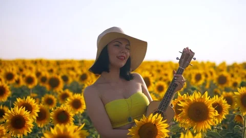 Happy woman in sunflower field playing on ukulele and singing. Summer girl in Stock Footage