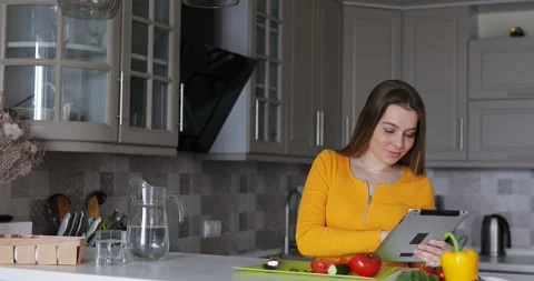 Happy woman use tablet computer smile at kitchen preparing dinner Stock Footage 135758196