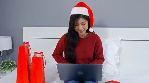 Happy woman using laptop computer and holding Christmas gift on a bed Stock Footage 97372202