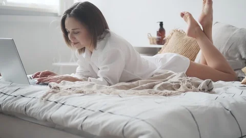 Happy woman is using laptop while lying in bed and smiling. girl in a man's Stock Footage 124796611