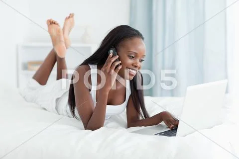 Happy woman using a laptop while making a phone call Stock Photos