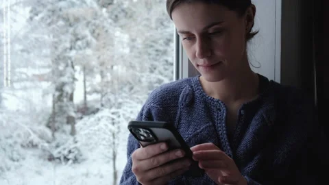 Happy woman in wintertime using smartphone sitting on cozy windowsill at home Stock Footage 226401445