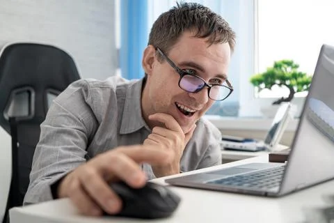 Happy worker smiling while using a laptop and computer mouse in office, enjoy Stock Photos