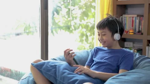 Happy young asian boy while connection on blue headphones is using a smartph Stock Footage 132085516