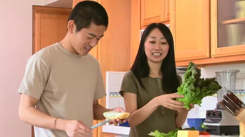 Happy young Asian couple preparing food in kitchen Stock Footage