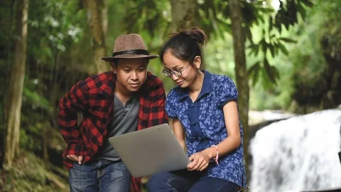 Happy young Asian couple using computer laptop near nature waterfall. 库存影片 96356778