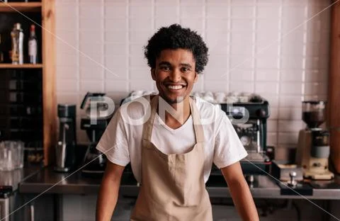 Happy young barista standing at cafe counter Stock Photos