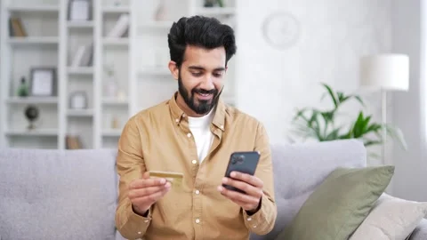 Happy young bearded man doing online shopping typing credit card number on smart Stock Footage 252213265