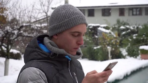 Happy young beautiful man using smartphone under the snow Stock Footage 82975107