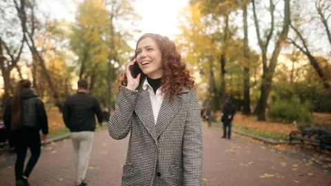 Happy young beautiful red-haired woman talking on mobile phone in autumn park Stock Footage 274067962