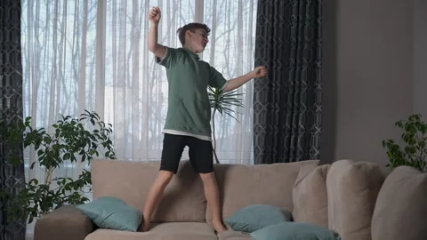 Happy young boy dancing on sofa, celebrating a win, having fun in living room. Stock Footage 270362258