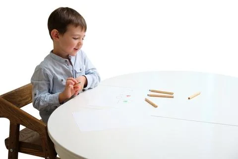 Happy young boy drawing with colored pencil on paper at table isolated on whi Stock Photos