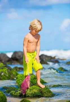 Happy young boy having fun at the beach, playing with fishing net, tropical v Stock Photos