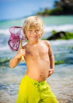 Happy young boy having fun at the beach, playing with fishing net, tropical v Stock Photos