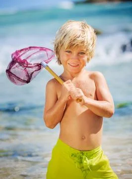 Happy young boy having fun at the beach, playing with fishing net, tropical v Stock Photos
