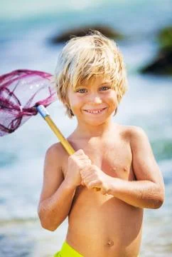 Happy young boy having fun at the beach, playing with fishing net, tropical v Stock Photos