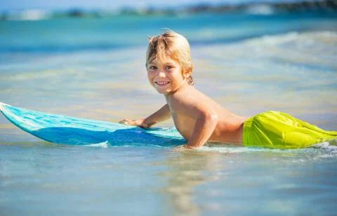 Happy young boy in the ocean on surfboard Stock Photos