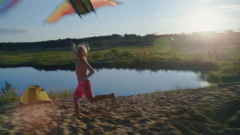 Happy young boy running and flying kite by the lake at sunset Stock Footage 344689557