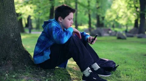 Happy young boy using smartphone in the park HD Stock Footage 10986838