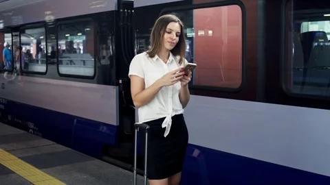 Happy, young businesswoman with smartphone standing at the railway station Stock Footage