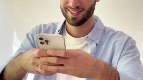 Happy young caucasian man with a beard, wearing a casual shirt, using a modern Vídeos de archivo 344756450