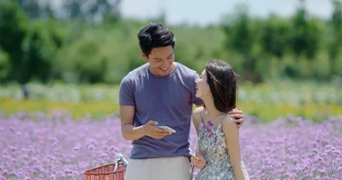 Happy young Chinese couple using smartphone in flower field,4K Stock Footage 119095458