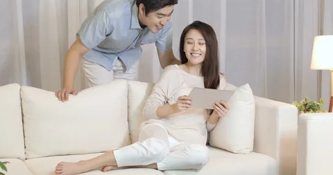 Happy young Chinese couple using digital tablet in living room,4K Stock Footage 151094743