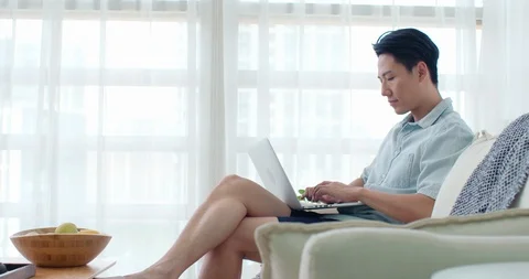 Happy young Chinese man using laptop in living room,4K Stock Footage 119037858