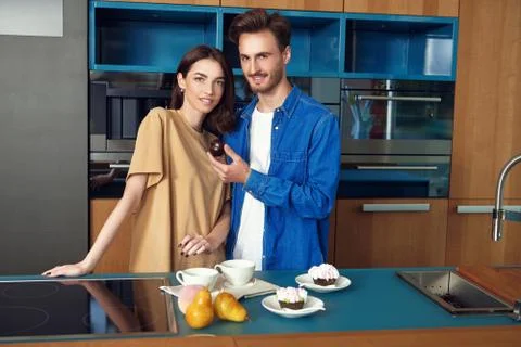 Happy young couple eating cakes in the kitchen at home. Home interior, furnit Stock Photos