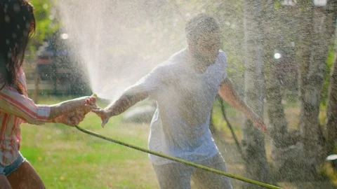 Happy Young Couple Has Fun on a Hot Summer Day Playing with Water Hose Sprinkler Stock Footage
