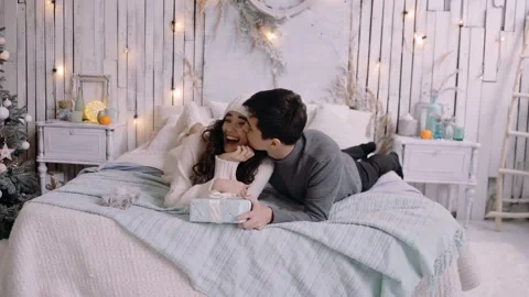 Happy young couple having fun on a comfortable bed, enjoying the Christmas Stock Footage 143750591