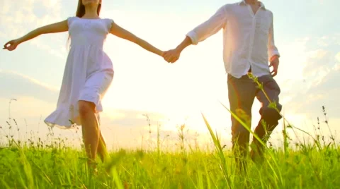 Happy young couple holding hands run through a wide field, having fun outdoors Stock Footage 59081929