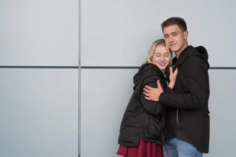 Happy young couple hugging while standing near gray wall Foto stock