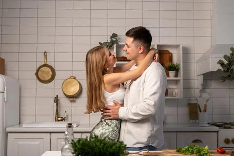 Happy young couple hugging while cooking at home. Handsome man and beautiful Stock Photos
