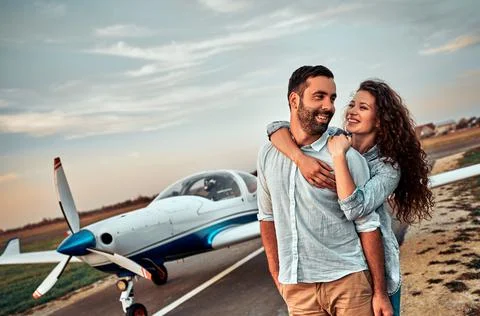Happy young couple laughing and having fun on runway near private aircraft Stock Photos