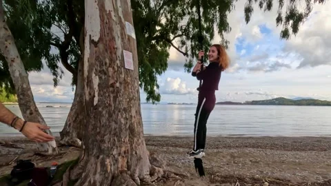 Happy Young Couple Playing on Rope Swing Under Large Tree by the Sea in Corfu Stock Footage 327785346