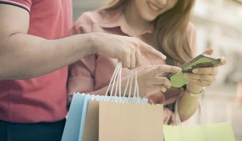 Happy young couple of shoppers walking in the shopping street towards and hol Stock Photos
