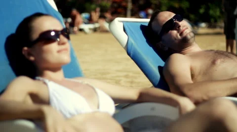 Happy young couple sunbathing on the beach, focus on man Stock Footage 1068573