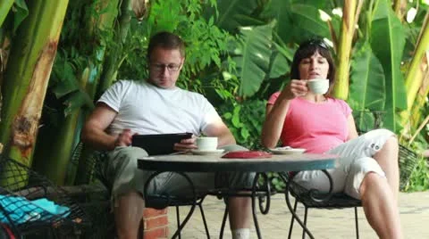 Happy young couple with tablet drinking coffee in bar, outdoors 스톡 동영상 10786538