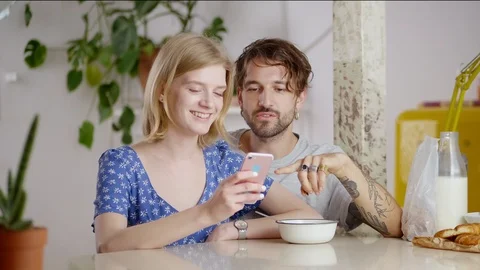 Happy young couple using pink smartphone together during breakfast in light Stock Footage 108797206