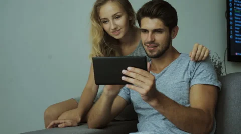 Happy young couple using a tablet, dressed in fashionable shirt on a brick wall Stock Footage 68720906