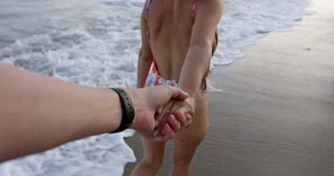 Happy young couple walking down beach - woman pulling mans hand as they walk  Stock Footage 94454064