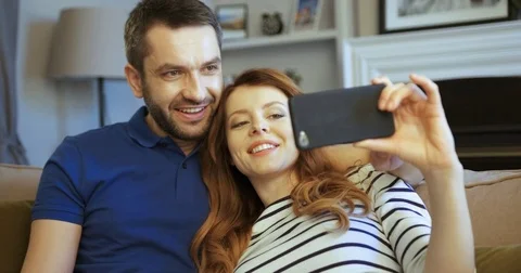 Happy young cuple relaxing on the sofa and taking selfies in a living room Stock Footage 74284774