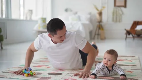 Happy young dad lying on floor carpet, lifting in air adorable little baby son Видео 153413969