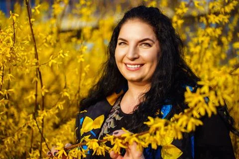 Happy young dark-haired plus size woman smiling happily in spring among yellow Stock Photos