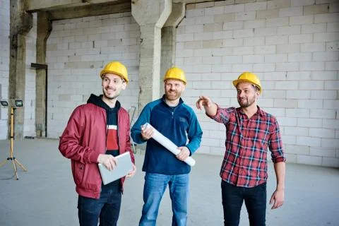 Happy young engineer in hardhat pointing at one of walls of unfinished building Fotos de archivo