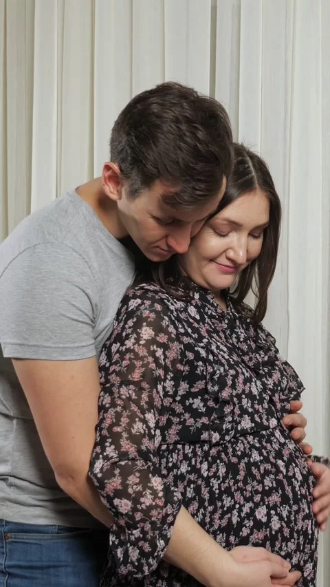 Happy young expecting couple hugging and caressing pregnant belly while standing Stock Footage 343909346
