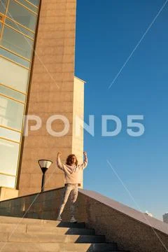 Happy young female sports winner with raised arms standing on marble staircase Stock Photos