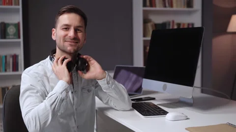 Happy young freelancer smiles taking off his headphones at workplace. Video stock 160556572